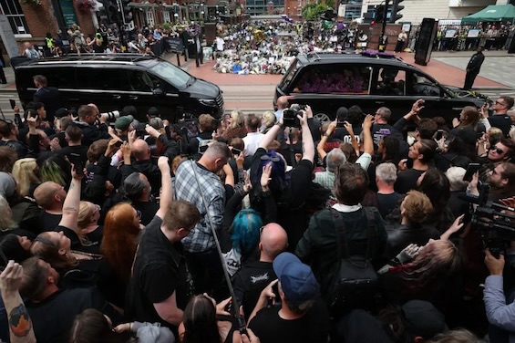 Photo of fans crowding hearses at a celebrity funeral in London like the one for the victim in this novel about odd couple detectives