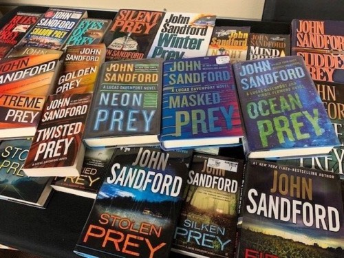 Photo of some of the many books in John Sandford's "Prey" series of detective novels like the one in this review, a novel about a murder conspiracy