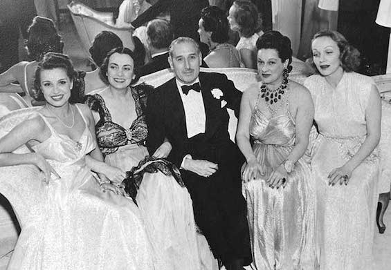 Photo of Sir Victor Sassoon surrounded by women in a night club. He was heir to a fortune built on trading opium. 